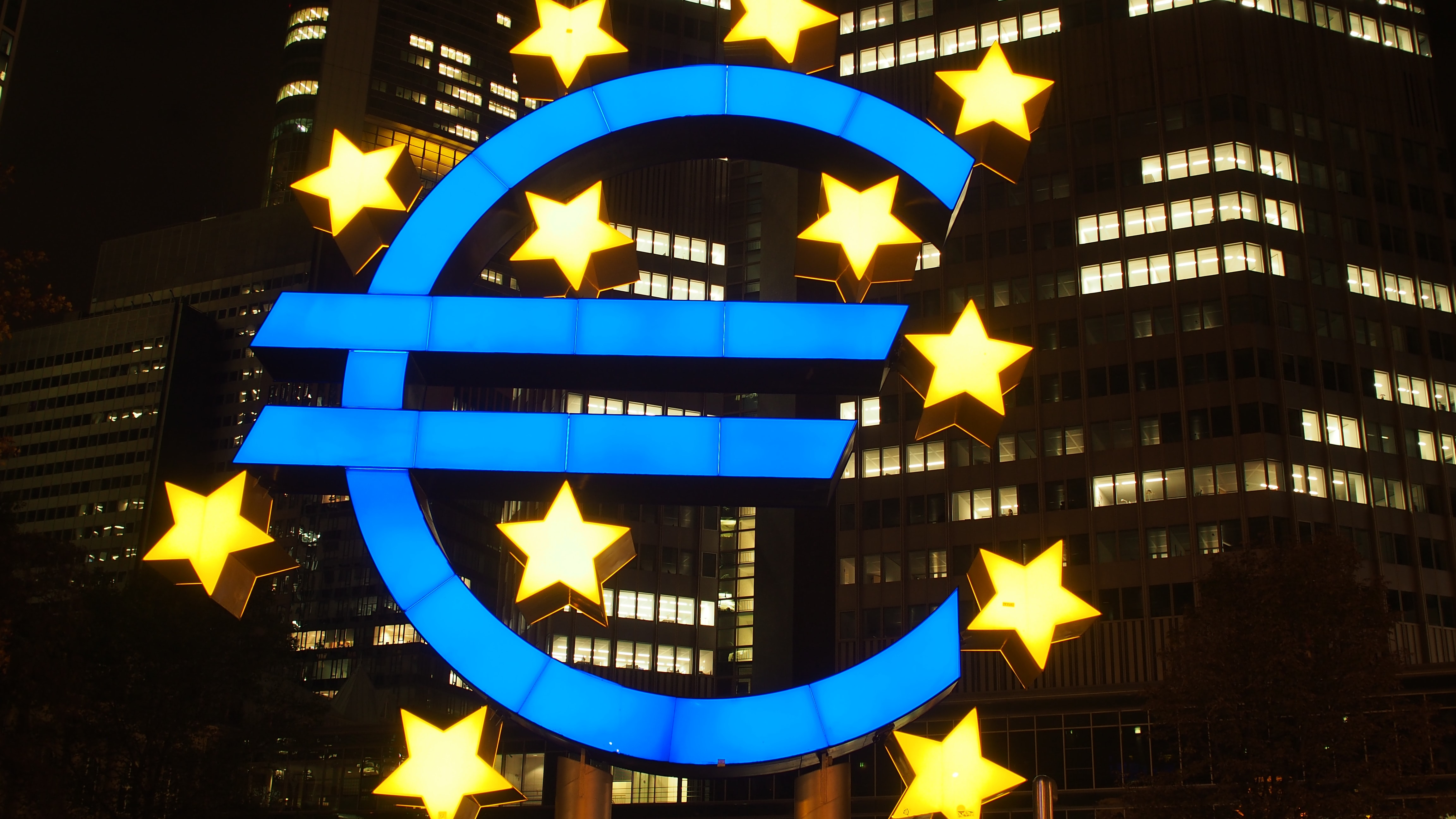 Illuminated Euro Symbol against City buildings