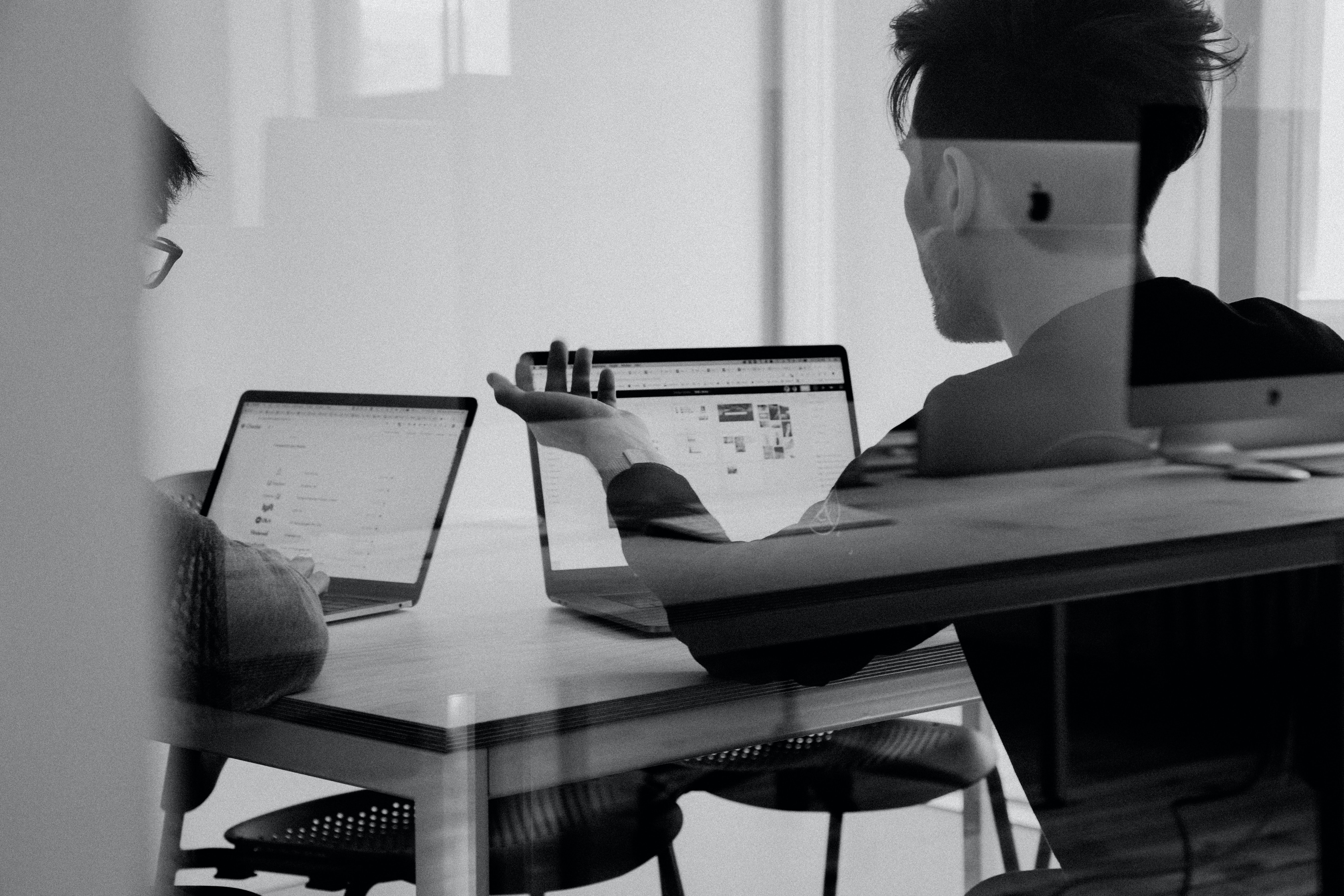 Two people discussing in front of laptops in black and white