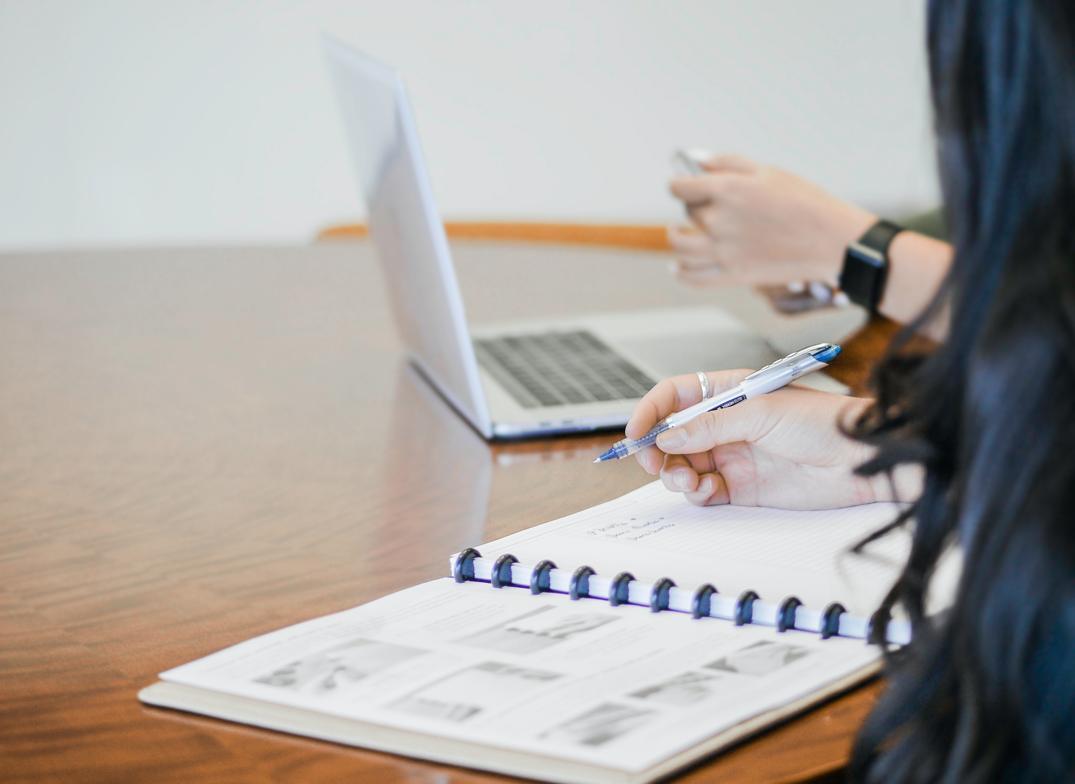 Closeup of team members taking notes on paper and laptop